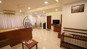 A modern living room with a wooden reception desk, a hanging chair, a TV, and a painting on the wall. - Hotel Kohinoor Square (Kolhapur)