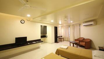 A hotel room with a bed, a desk, a chair, a television, a clock, and an air conditioning unit.
