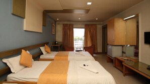 A hotel room with two beds, a TV, a desk, and a view of the outdoors. - Hotel Kohinoor Square (Kolhapur)
