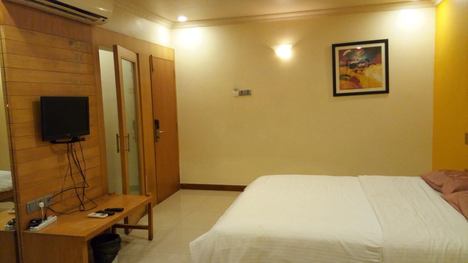 A hotel room with a bed, a desk with a TV, a mirror, and a painting on the wall.