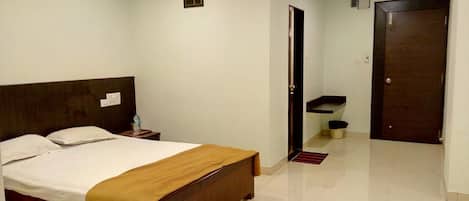 A hotel room with a bed, a nightstand, a small table, a door, and a trash bin.