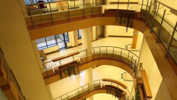 A multi-level atrium with glass railings and wooden accents, featuring a central open space and multiple balconies. - Hotel Kohinoor Square (Kolhapur)