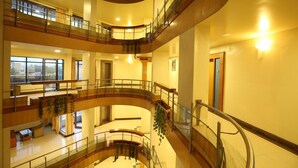 A multi-level atrium with curved balconies, glass railings, and indoor plants. - Hotel Kohinoor Square (Kolhapur)
