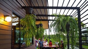 A covered outdoor seating area with hanging plants and a view of a water body. - Green 2 (Chanthaburi)