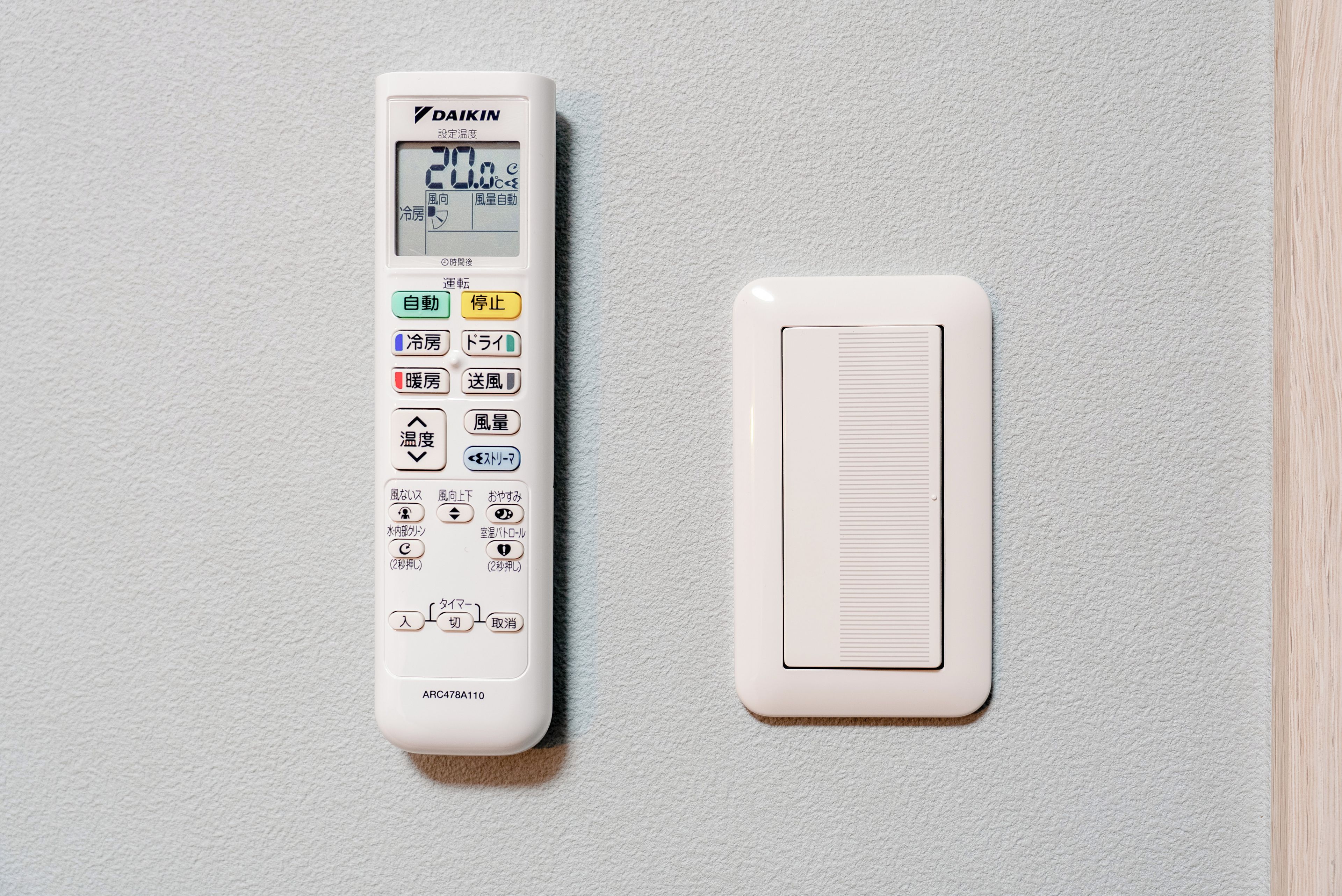 A white Daikin air conditioner unit with a digital display and control panel, and a white vent on a textured wall.