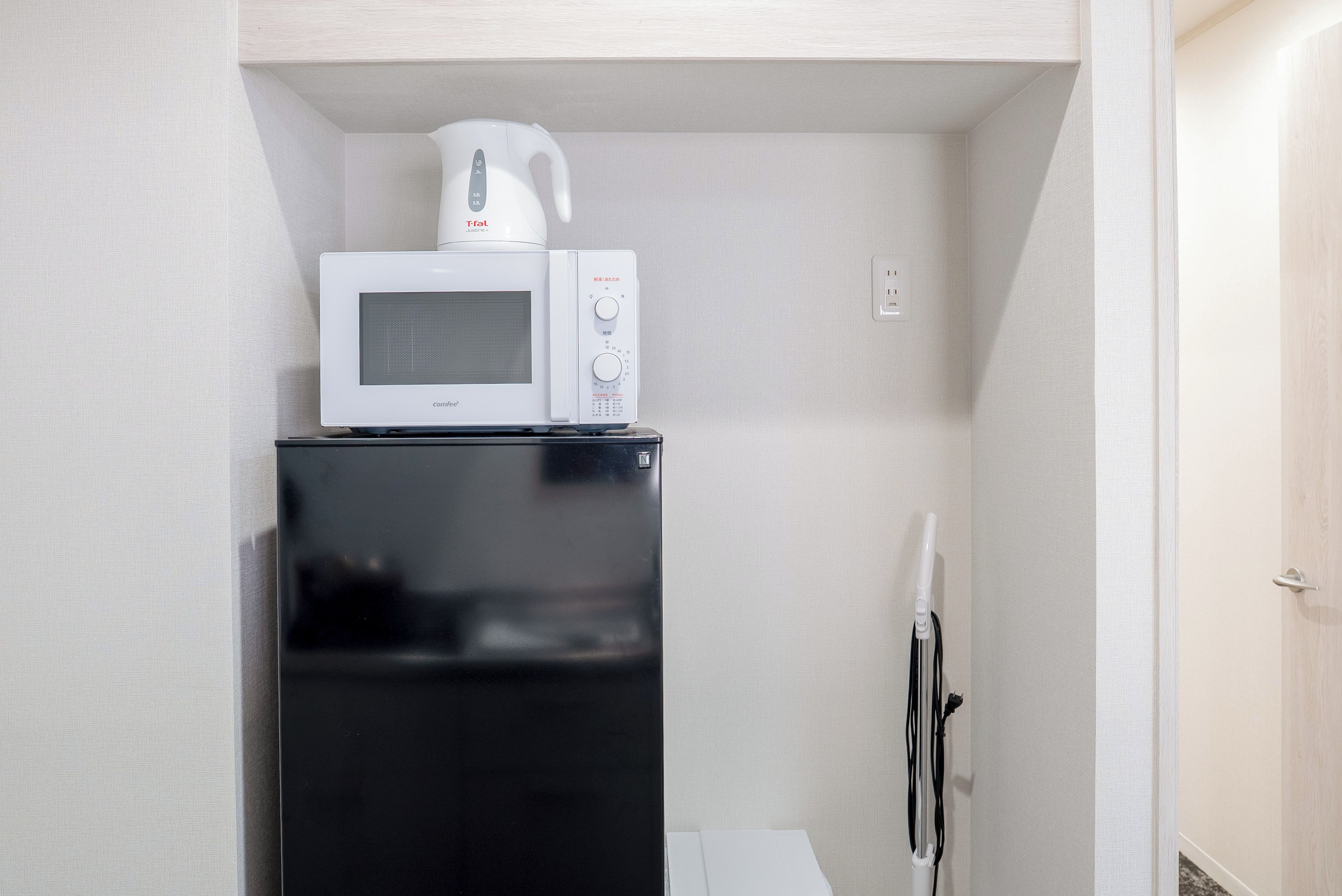 A compact kitchenette with a black refrigerator, a white microwave, and a kettle.