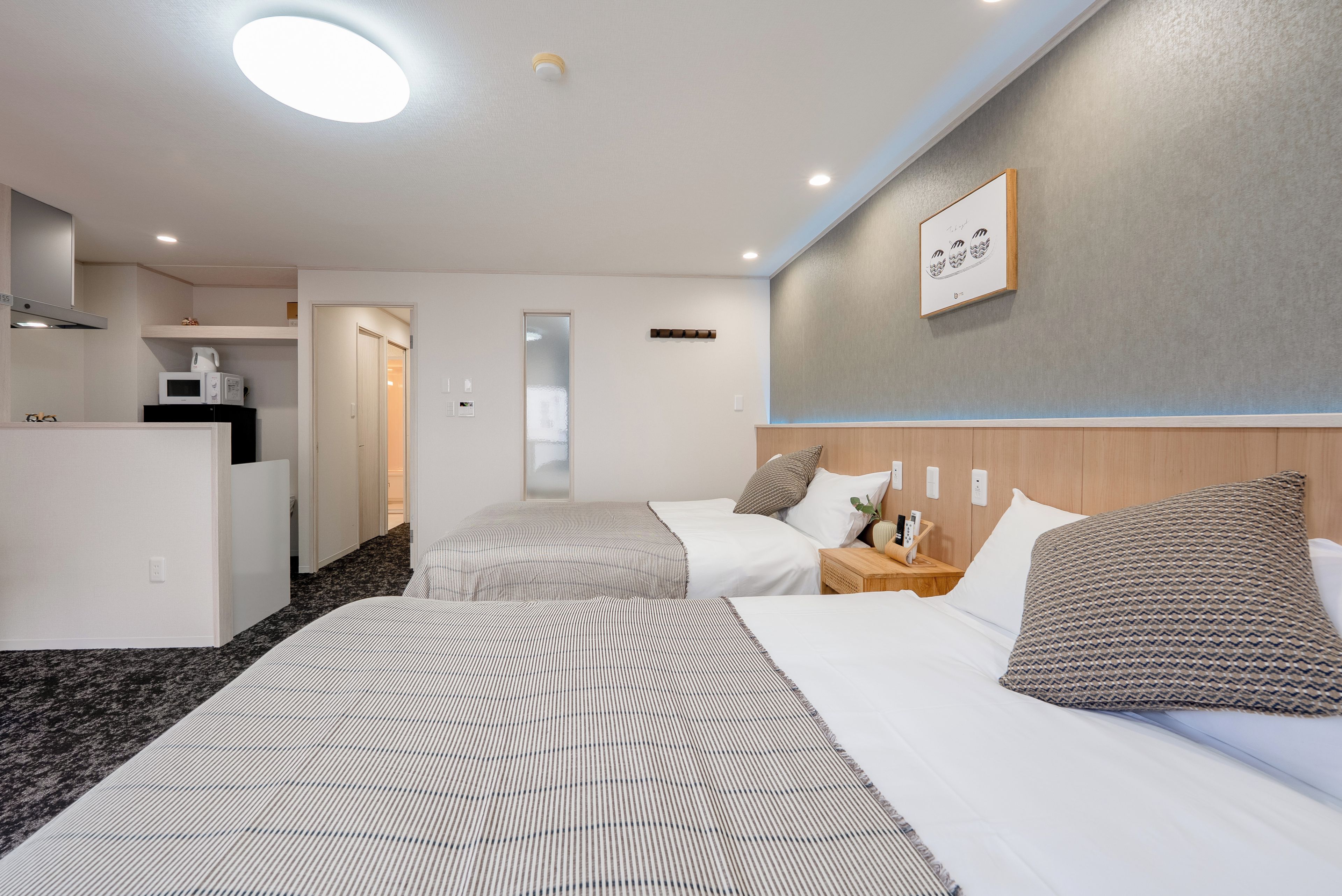 A hotel room with two beds, a kitchenette, and a bathroom.
