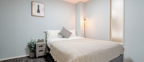 A bedroom with a bed, bedside table, lamp, and a framed picture on the wall.