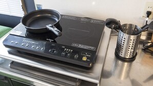 An induction cooktop with a frying pan and a colander on a stainless steel countertop.