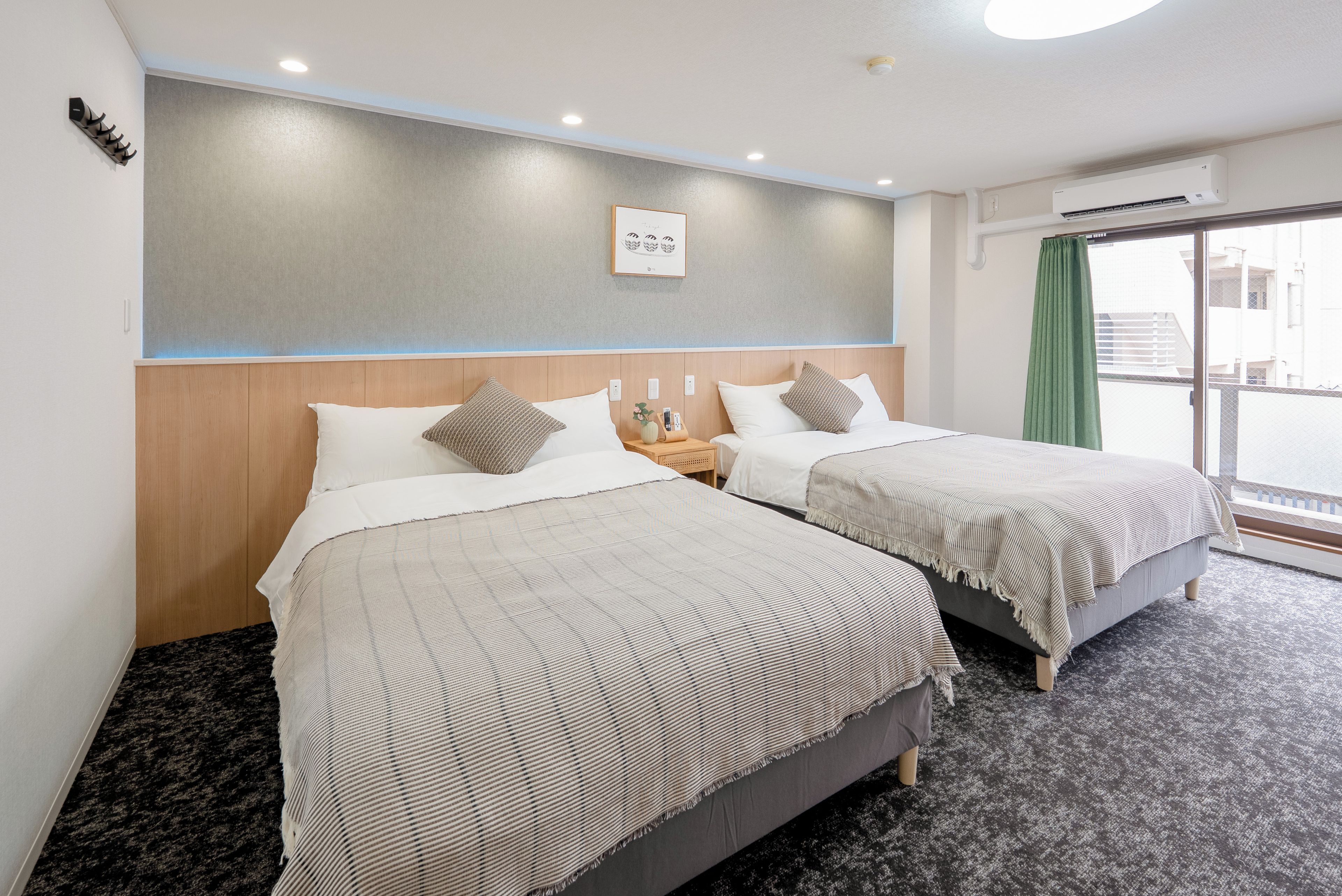 A hotel room with two beds, a small bedside table, a wall-mounted picture, and a window with a view.