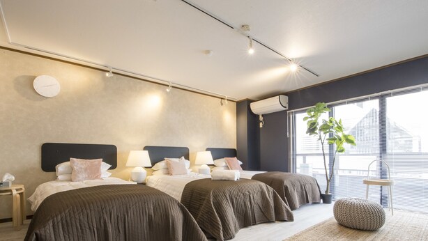 A modern hotel room with a large bed, bedside tables, lamps, and a large window with blinds.