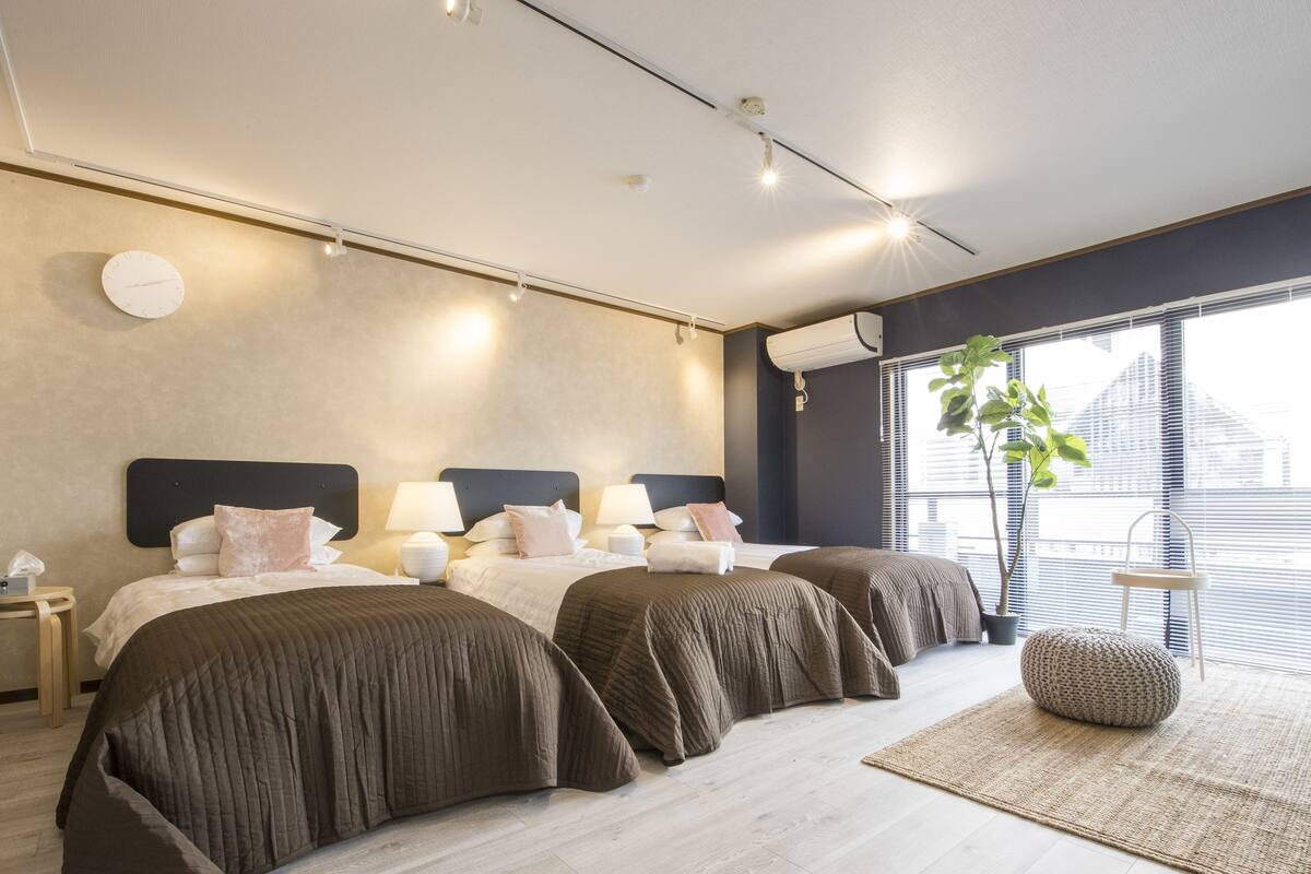 Una habitación de hotel moderna con una cama grande, mesitas de noche, lámparas y un ventanal con persianas.