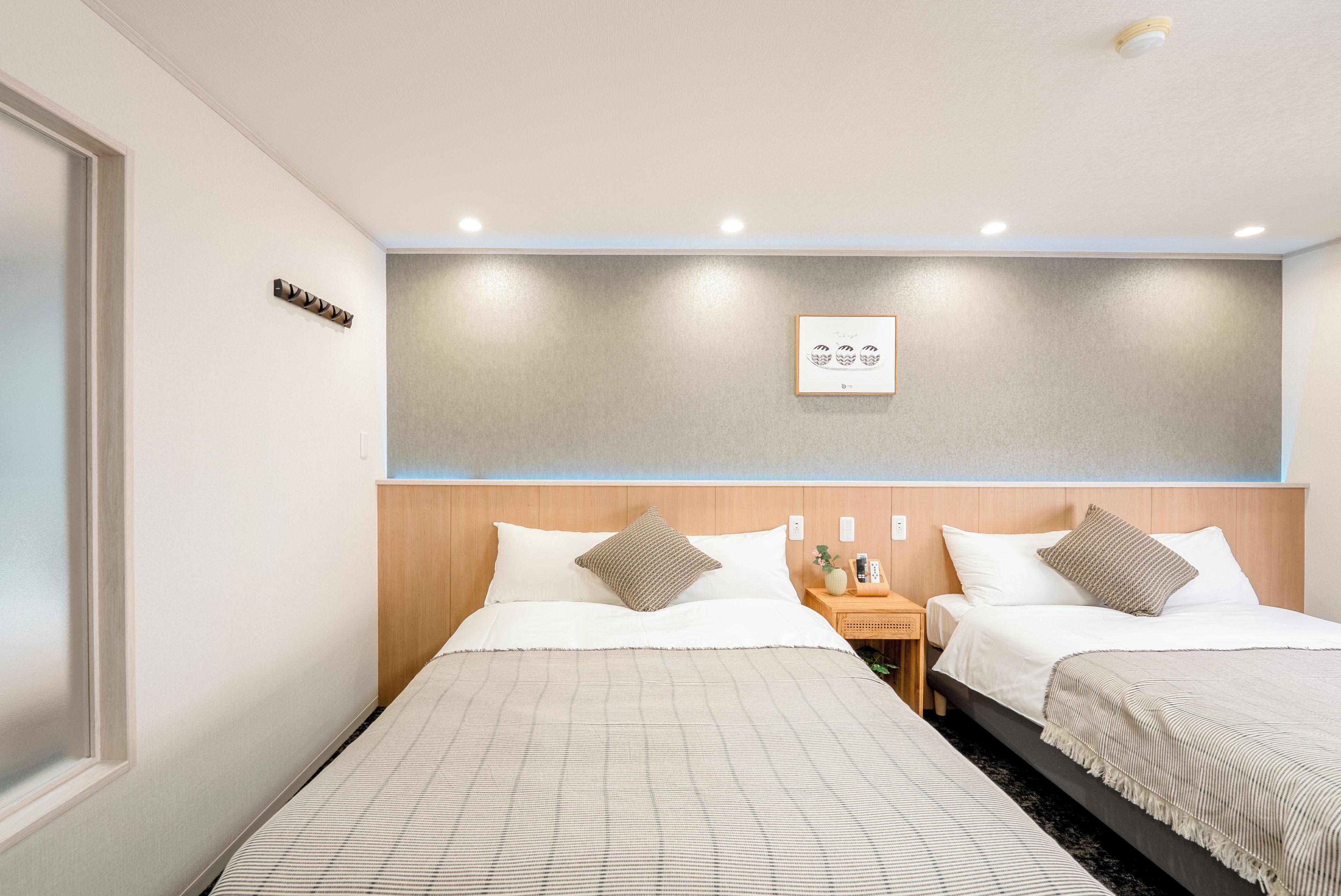 A hotel room with two beds, a bedside table with a phone and a vase, and a wall-mounted light fixture.
