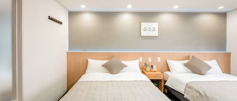A hotel room with two beds, a bedside table with a phone and a vase, and a wall-mounted light fixture.