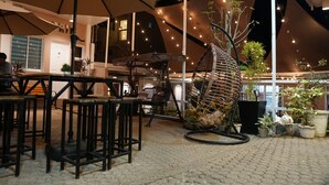 Un área de estar al aire libre con mesas y sillas, un paraguas grande e iluminación decorativa.