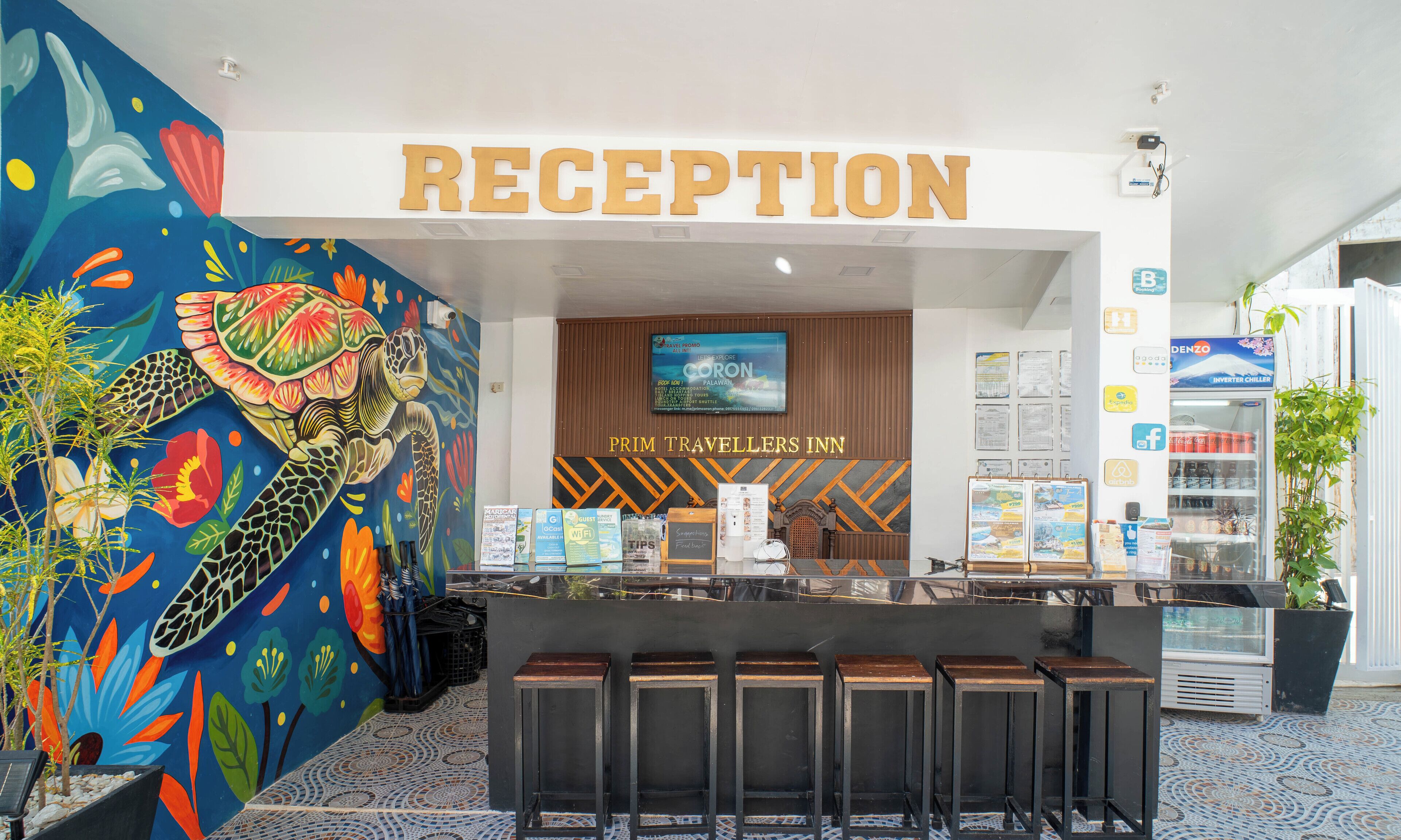 Zona de recepción con un mural colorido, un cartel que dice "RECEPTION" y un mostrador con folletos informativos.