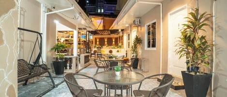 An outdoor patio area with a round table and chairs, potted plants, and a view of a building in the background.