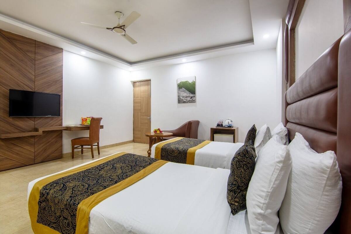 A hotel room with two beds, a desk, a chair, a television, and a ceiling fan.