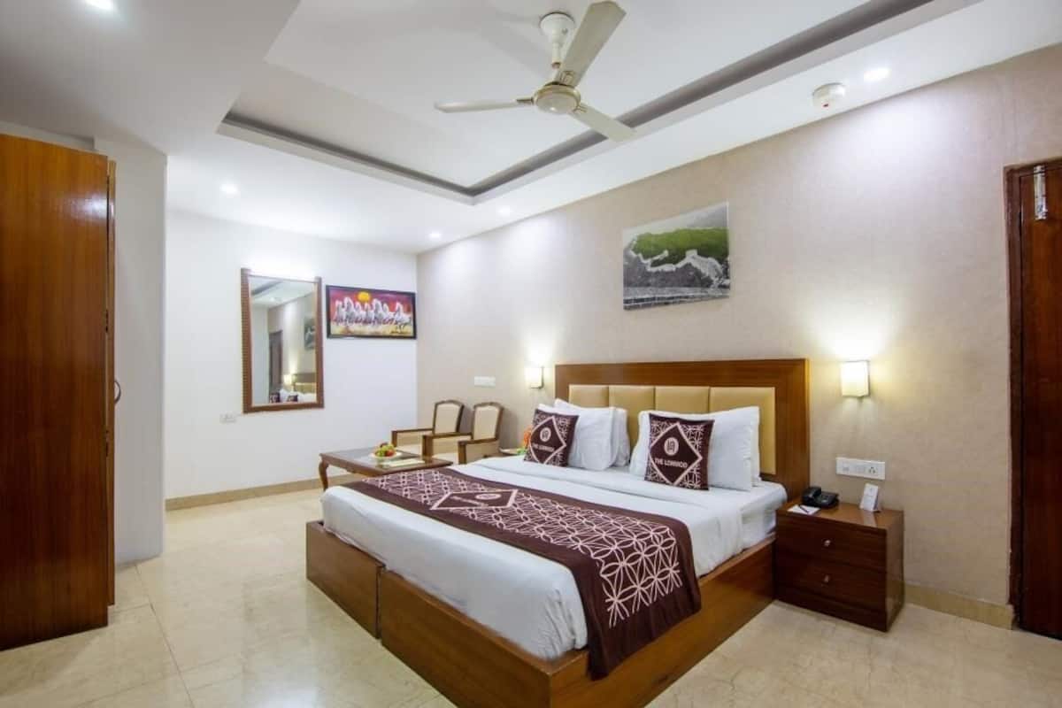 A hotel room with a large bed, a bedside table, a nightstand, a ceiling fan, and a painting on the wall.