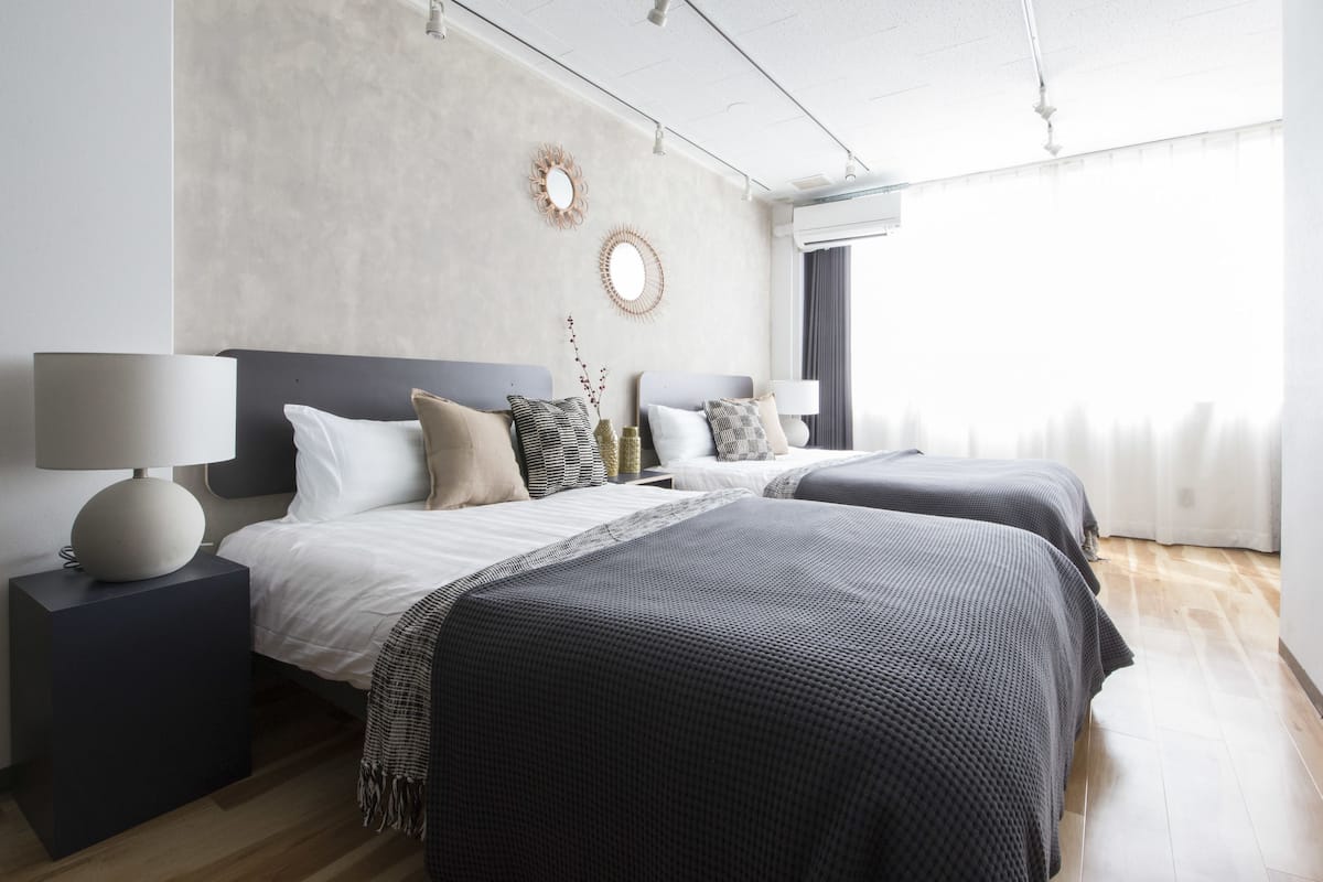 A modern hotel room with two beds, a large mirror, and a view of the city.