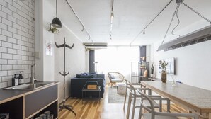 A modern kitchen with a wooden floor, a dining area with white chairs, and a black sofa. - nid NAMBA Station House (Osaka)