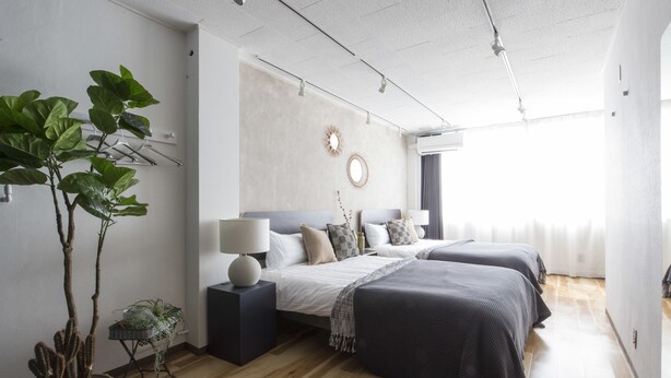 A modern bedroom with two beds, a large potted plant, a mirror, and a wall-mounted air conditioner. - nid NAMBA Station House (Osaka)