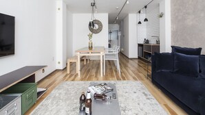 A modern living room with a flat-screen TV, a dark sofa, a wooden dining table with chairs, and a kitchen area with a sink and countertop. - nid NAMBA Station House (Osaka)