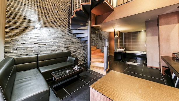 A modern interior with a black leather sofa, a wooden dining table, and a spiral staircase leading to an upper level. - Arrietty Motel (Gyeongju)