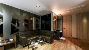 A modern living room with a sectional sofa, a coffee table, and a TV. There is a wooden floor and a large mirror. - Arrietty Motel (Gyeongju)