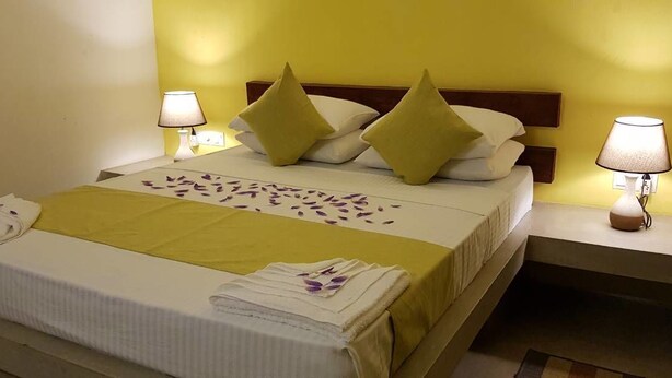 A neatly made bed with a yellow bedspread, white linens, and decorative pillows. There are two bedside lamps on either side of the bed. - Villa Tulip Garden (Anuradhapura)