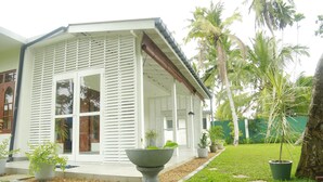 A modern house with a covered porch, large windows, and a well-maintained garden with palm trees and potted plants. - Villa A.SMS (Induruwa)