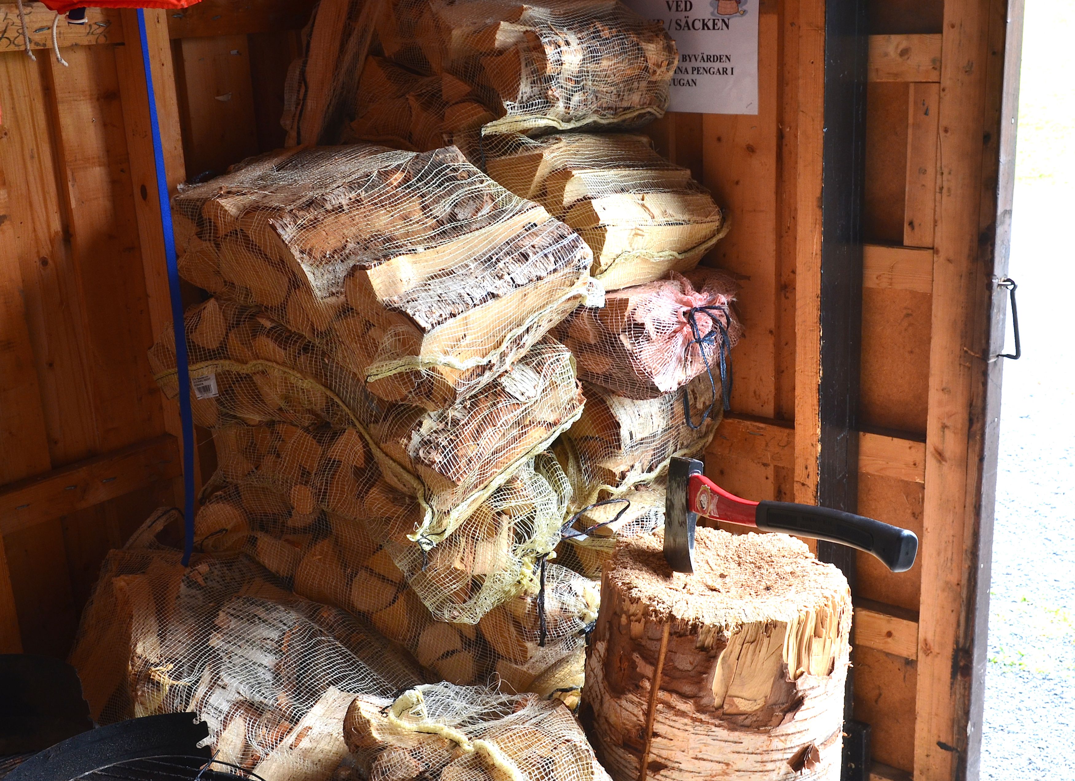 A storage area with stacks of burlap sacks containing logs, a saw, and a sign with text.