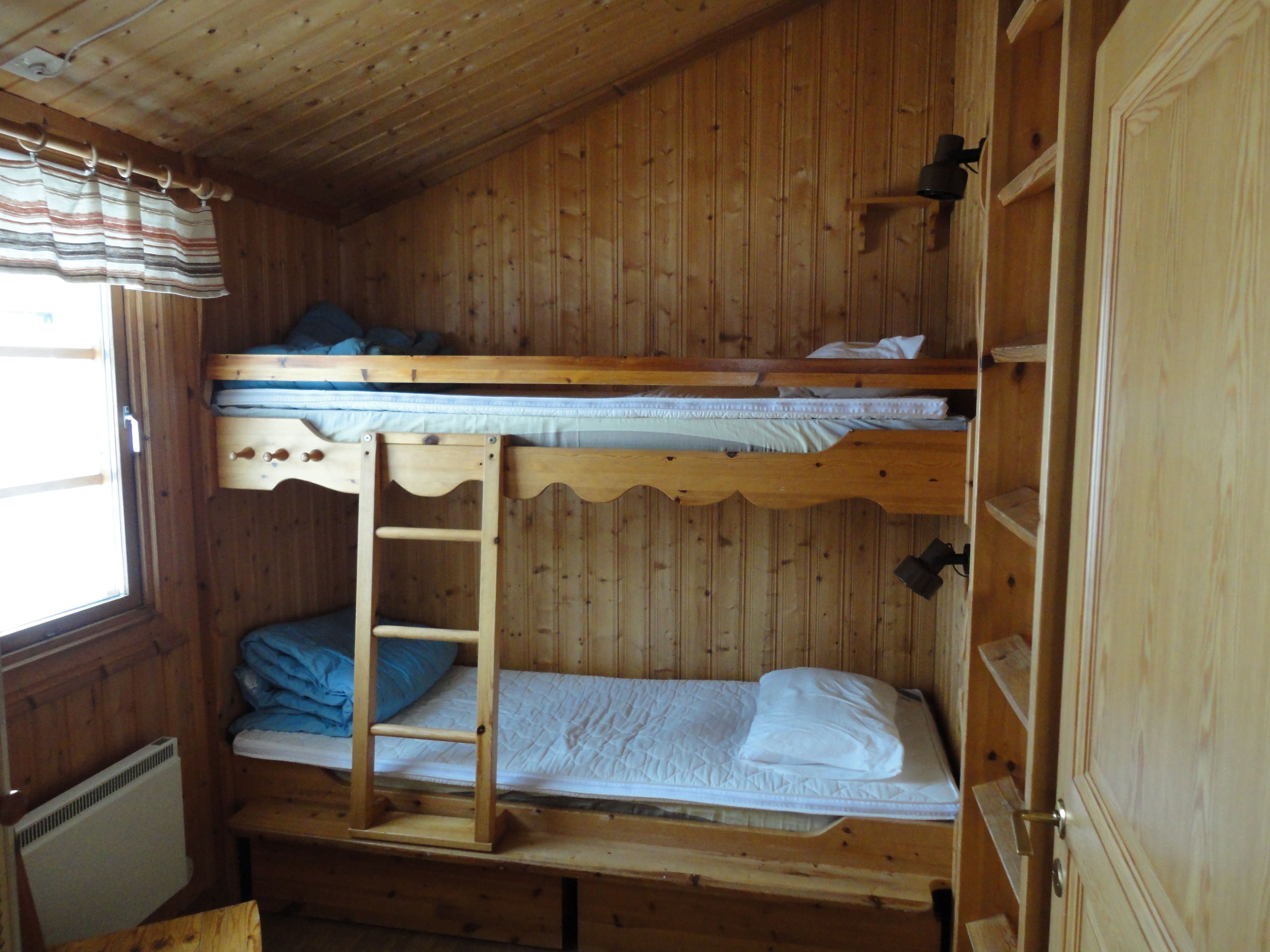 Habitación con literas, una escalera, paredes de madera y una ventana con cortinas.