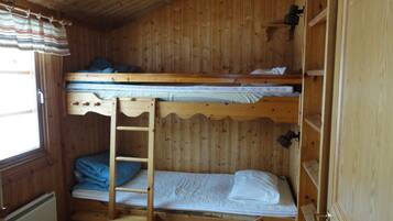 Habitación con literas, una escalera, paredes de madera y una ventana con cortinas.