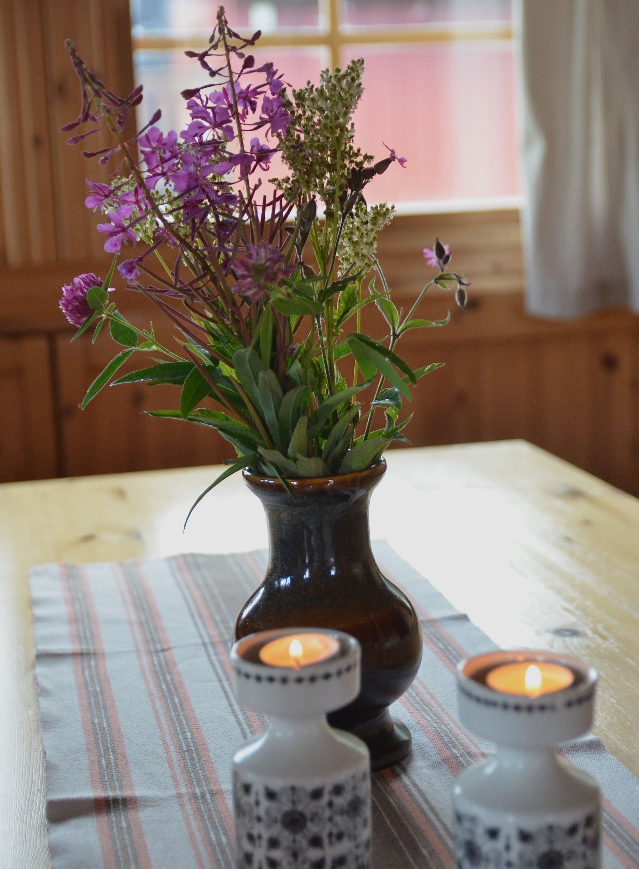 A wooden table with a vase of purple flowers and two candle holders.