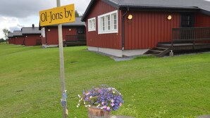A red building with a sign reading "Ol-Jons by" and a flower pot in the foreground. - Ol-jons By (Hallen)
