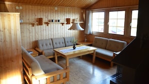 A cozy cabin interior with wooden walls, a sofa, a table, and a fireplace. - Ol-jons By (Hallen)