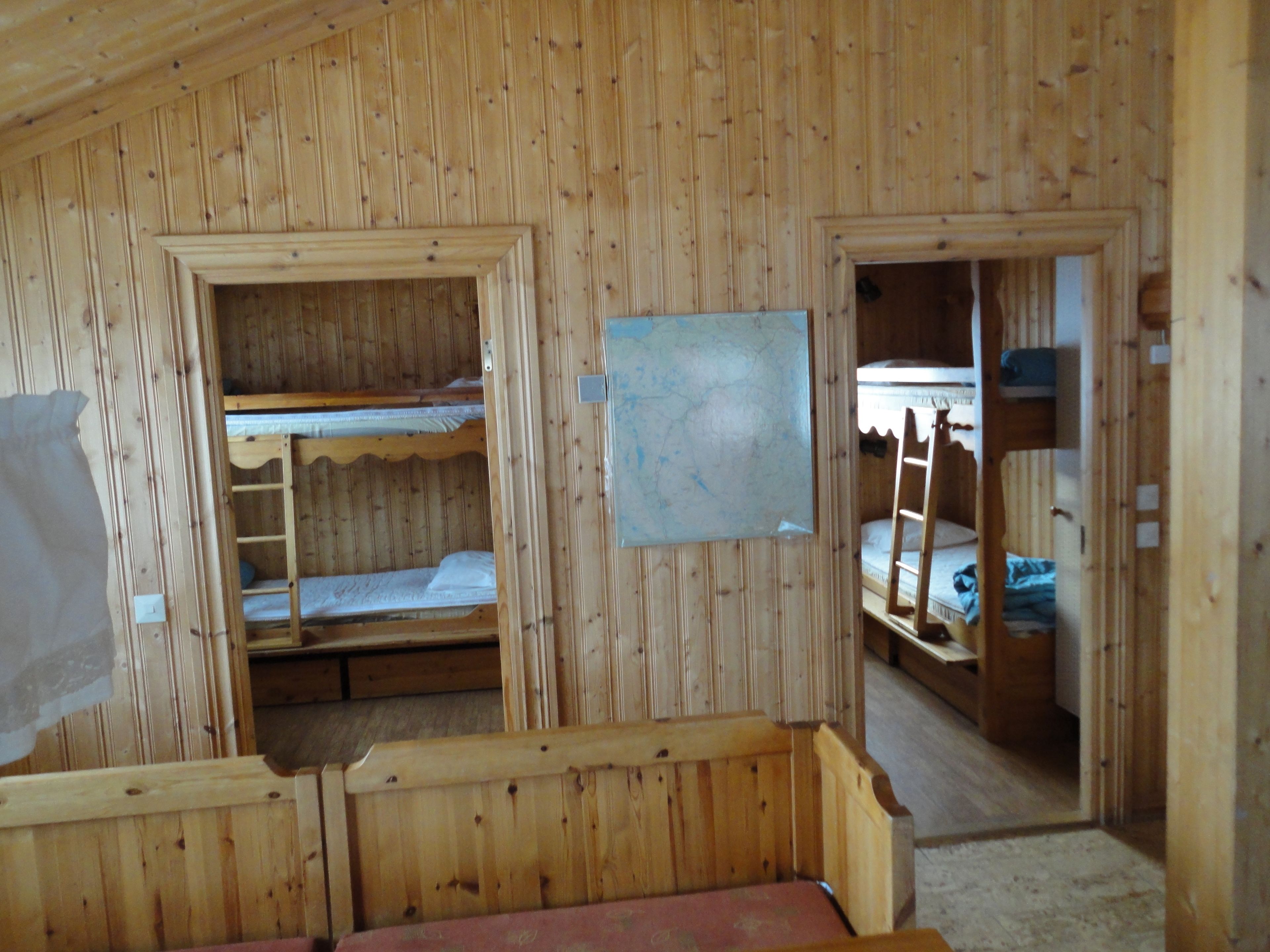 Una cabaña de madera con literas, una mesita y una lámpara fijada a la pared.
