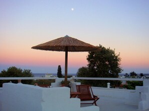 A sunset view from a balcony with a thatched umbrella, white walls, and a wooden chair. - Blugreen Stegna B&B (Rhodes)