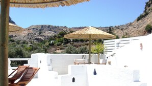 A white-walled terrace with a wooden lounge chair and a thatched umbrella, overlooking a mountainous landscape. - Blugreen Stegna B&B (Rhodes)