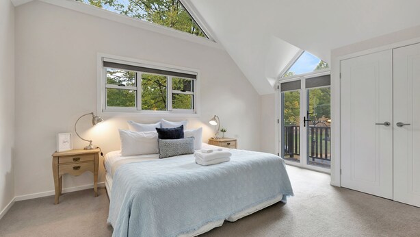 A bedroom with a large bed, two bedside tables, a window, and a sliding glass door to a balcony. - Beyond Bliss - Guesthouse 1 (BRIGHT)