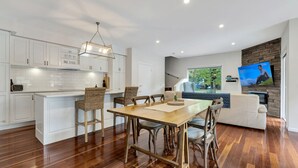 A modern kitchen with white cabinets, a wooden dining table, and a stone fireplace. - Beyond Bliss - Guesthouse 1 (BRIGHT)