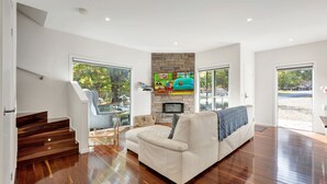 A modern living room with a stone fireplace, a large TV, and a sofa. - Beyond Bliss - Guesthouse 1 (BRIGHT)