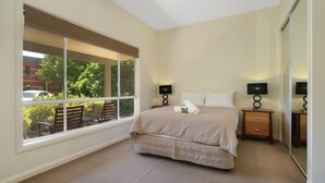 Une chambre avec une grande fenêtre, un lit, deux tables de chevet avec des lampes et une vue sur l’extérieur.