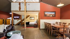 A rustic interior with a dining area, a loft bedroom, and a TV in the background. - Quins Gap Escapes (Bright)