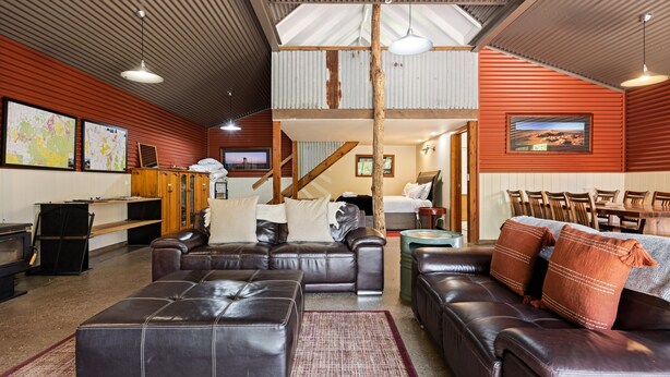 A spacious living room with leather sofas, a dining area, and a staircase leading to an upper level. - Quins Gap Escapes (Bright)