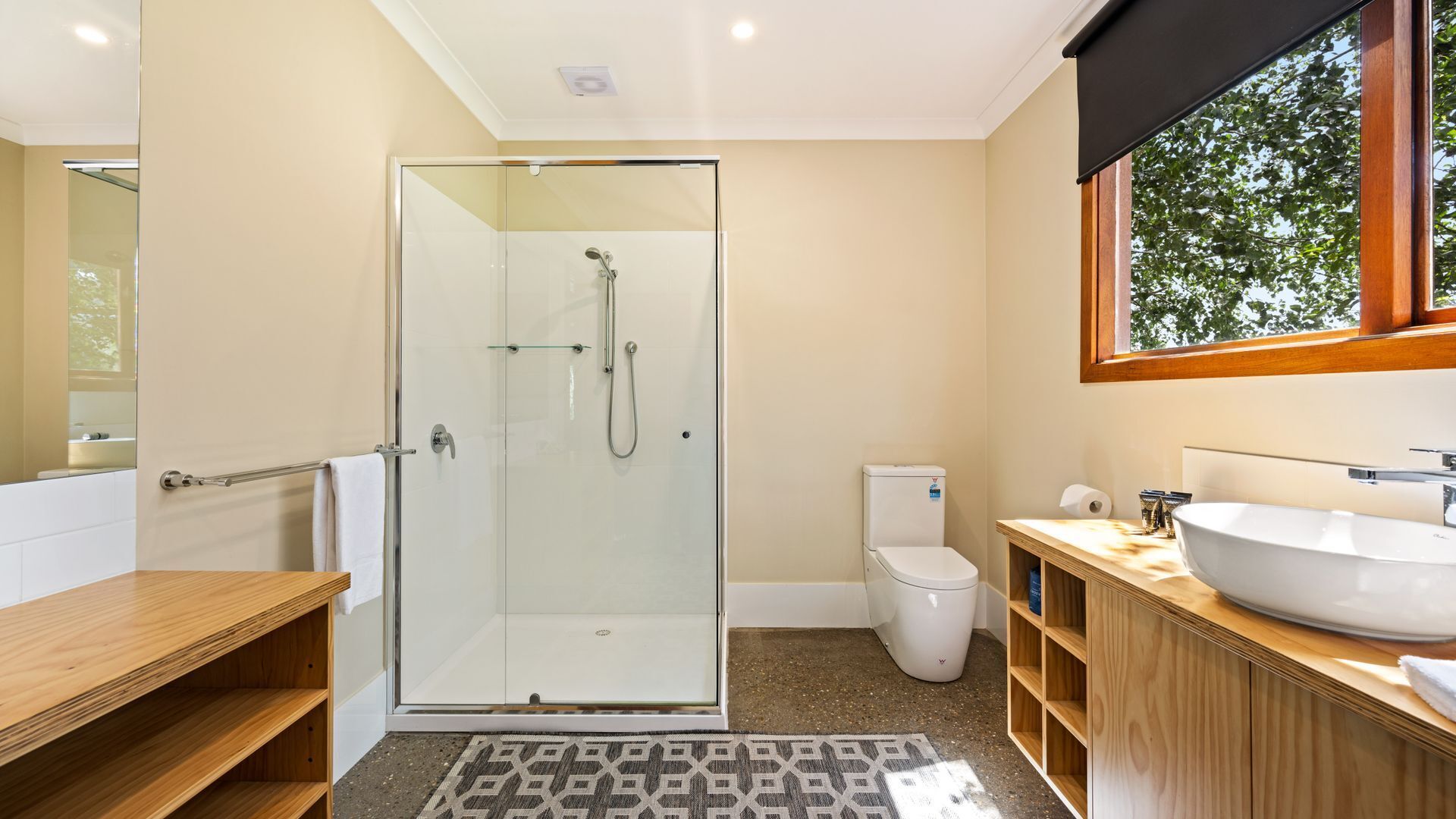 Een moderne badkamer met een douchecabine van glas, een toilet, een wastafel en een houten opbergmeubel.