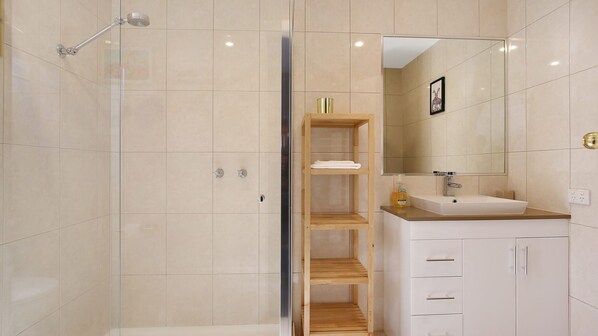 A modern bathroom with a walk-in shower, a wooden shelf unit, a sink with a mirror, and a toilet.