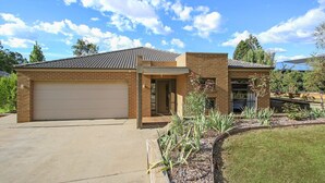 A two-story house with a garage, a brick exterior, and a landscaped front yard. - Always Bright - A Bright Escape (BRIGHT)