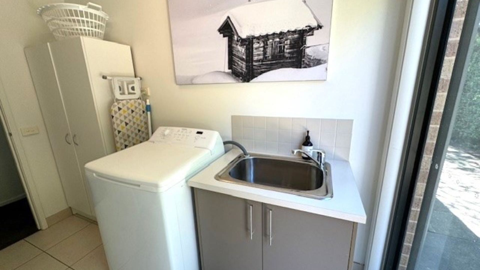 Une cuisine de taille réduite, équipée d’un lave-linge, d’un évier et d’un petit placard.